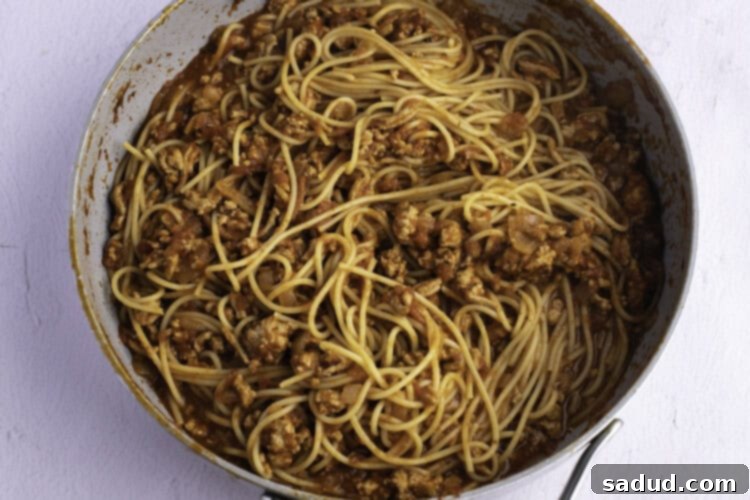 Overhead view of turkey spaghetti with red sauce in a large skillet on a white background.
