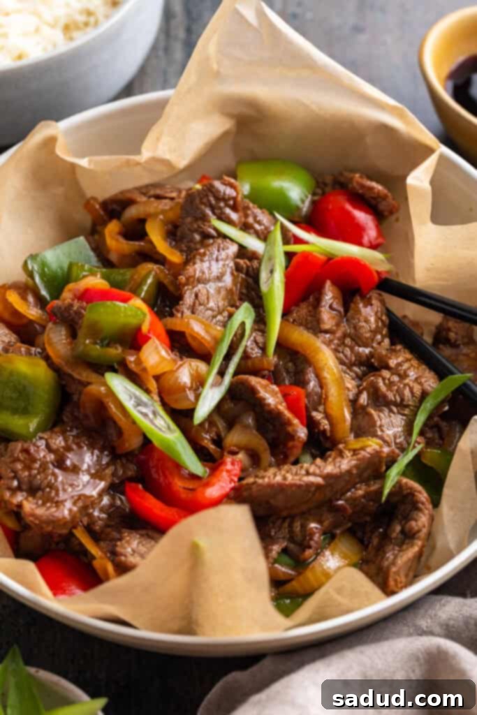 Tender slices of beef with vibrant bell peppers and onions coated in a rich oyster sauce, served in a large silver bowl on parchment paper.
