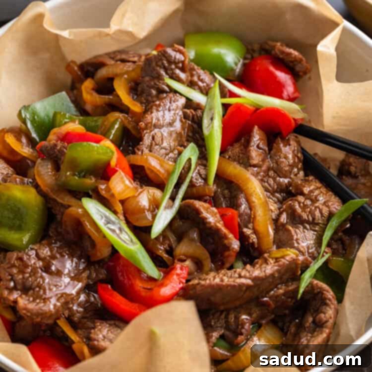 Beef with veggies and oyster sauce in a large silver bowl with parchment paper, garnished with green onions.