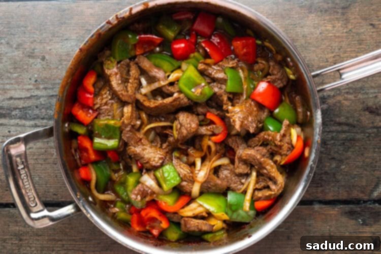 Beef with oyster sauce and stir-fried vegetables in large silver saucepan sitting on a wooden background, fully cooked and ready to serve.
