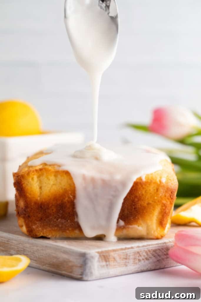 Irresistible Gluten-Free Lemon Cake 3 Thick, glossy lemon glaze being artistically poured over a freshly baked gluten-free lemon pound cake loaf, with a soft floral background of tulips.