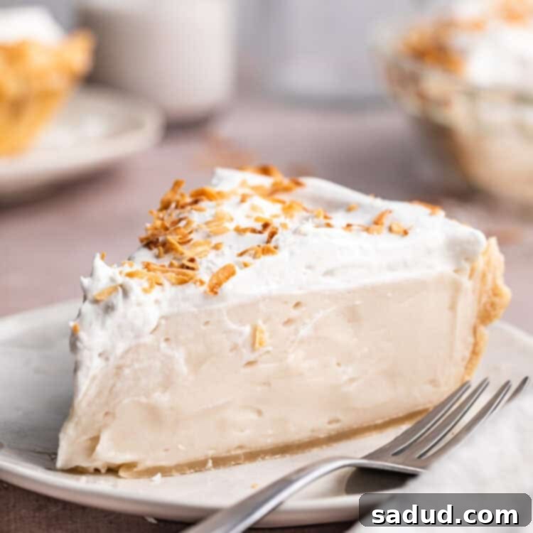 A wedge sliced of vegan coconut cream pie topped with coconut whipped cream and coconut shavings on a neutral plate with a fork.