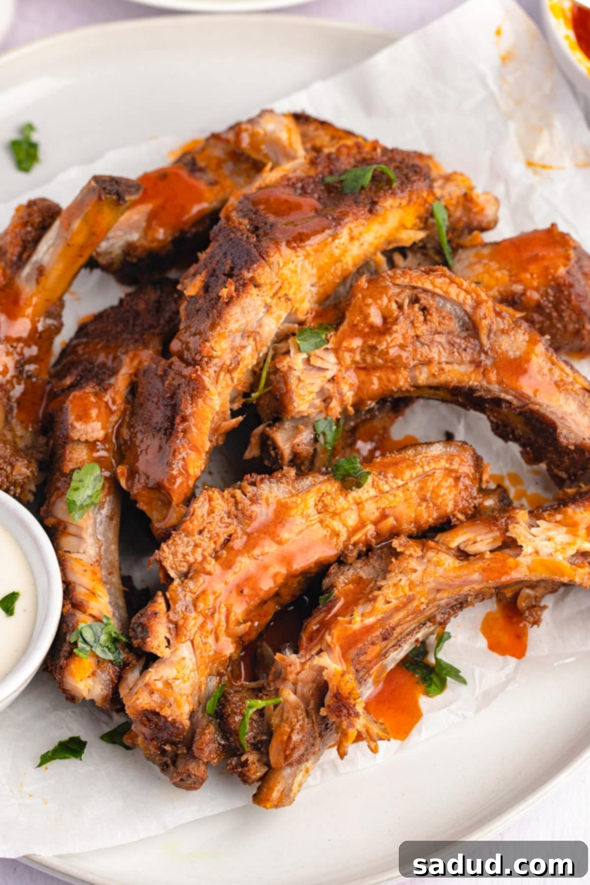 A pile of baked buffalo ribs with bbq sauce on a white plate, with a focus on the saucy texture.