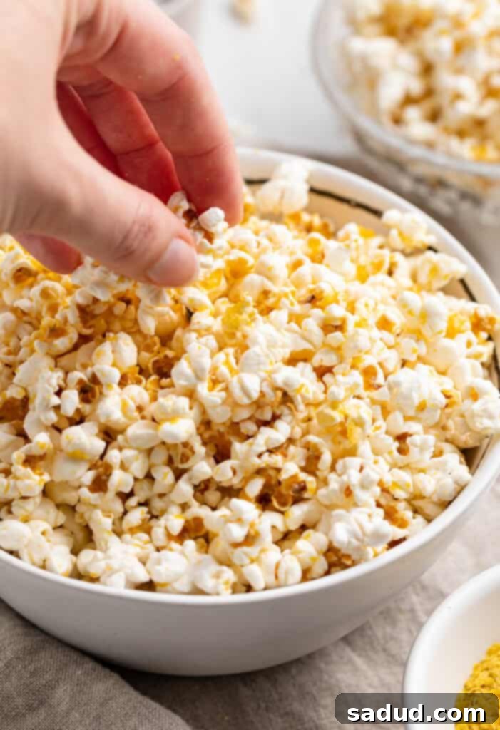 A hand picking up buttery vegan popcorn from a large bowl of vegan popcorn.