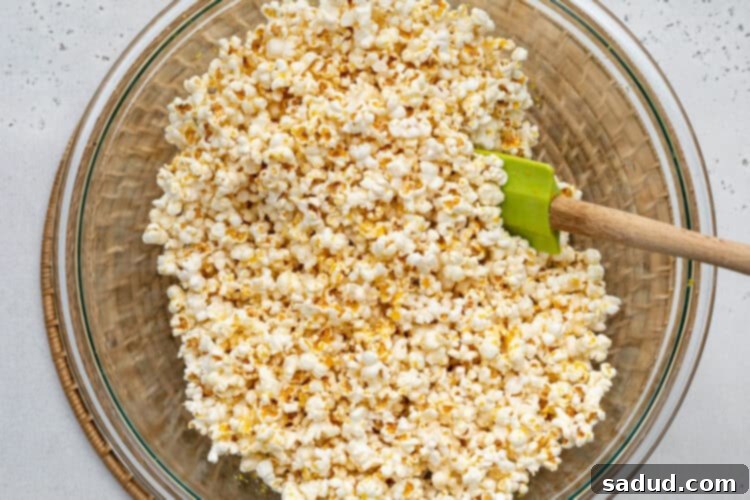 Overhead view of vegan buttery popcorn in a large silver bowl with a rubber spatula.
