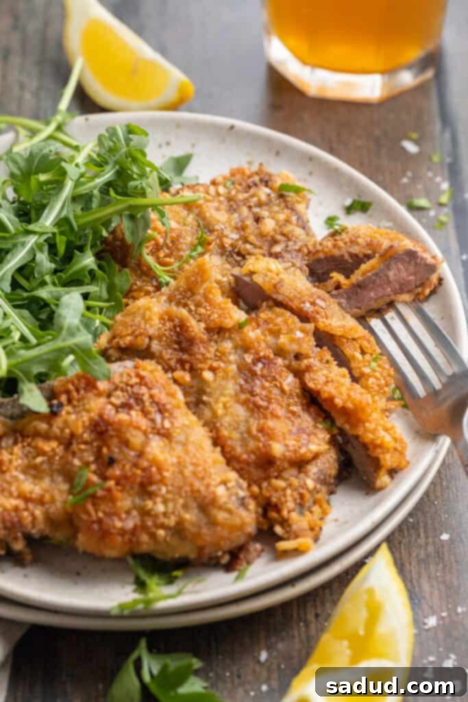Overhead, angled, zoomed out view of crispy beef schnitzel plated with a fresh salad of microgreens and a wedge of lemon, highlighting a light and healthy serving suggestion.