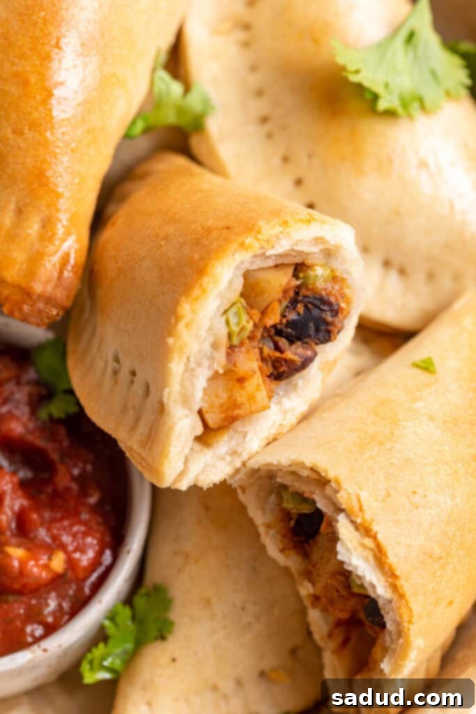 Irresistible Vegan Empanadas 2 Overhead view of a pile of vegan empanadas next to a small bowl of salsa, with one empanada torn in half to show insides.