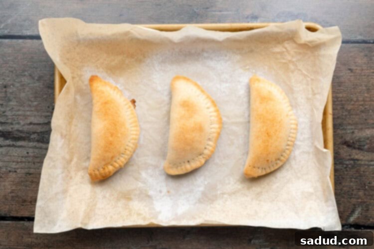 Irresistible Vegan Empanadas 12 Overhead view of baked empanadas on a baking sheet lined with parchment paper.