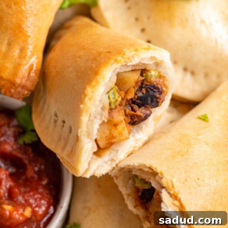 Irresistible Vegan Empanadas 4 Overhead view of a pile of vegan empanadas next to a small bowl of salsa, with one empanada torn in half to show insides.
