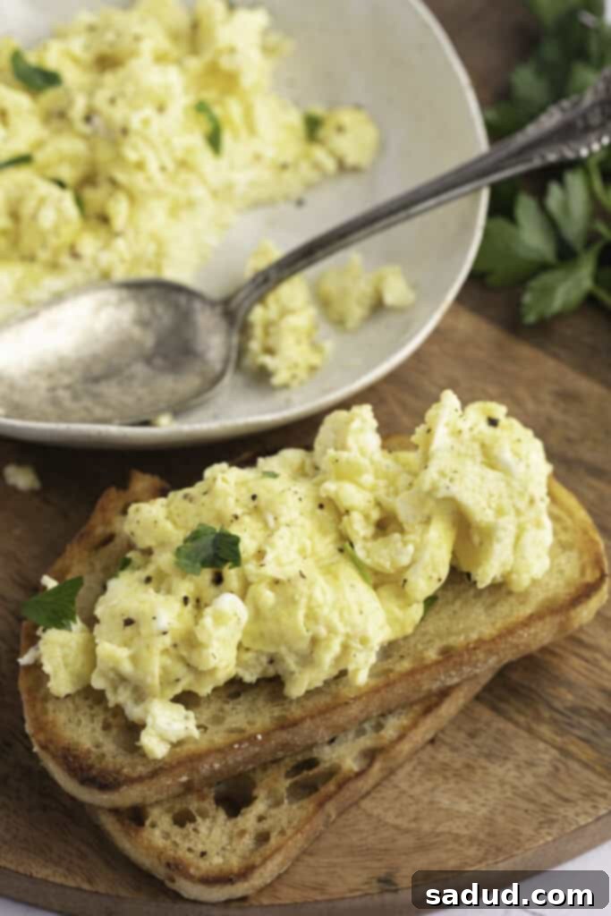 Fluffy Instant Pot Scrambled Eggs 2 Angled view of Instant Pot scrambled eggs on toast, resting on a wooden cutting board, garnished with fresh herbs.