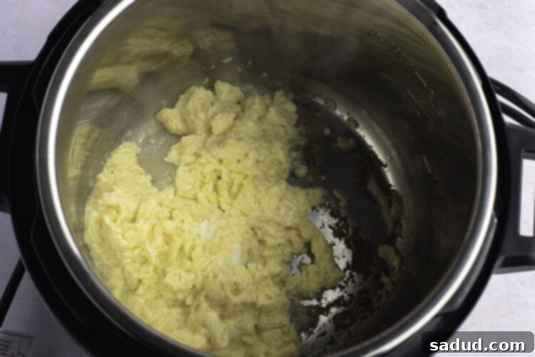 Overhead view of perfectly cooked fluffy scrambled eggs in an Instant Pot, being gently stirred with a spatula.