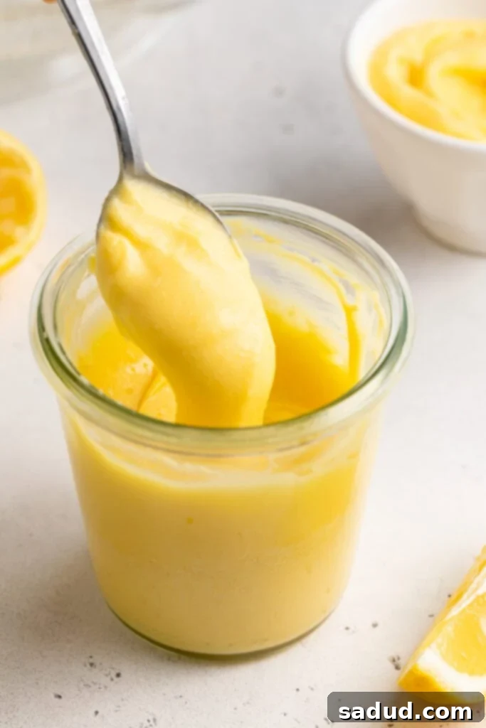 Effortless Keto Lemon Curd Four Ingredients 2 3/4-angle view of a small glass of keto lemon curd, with a silver spoon lifting lemon curd out of the glass.