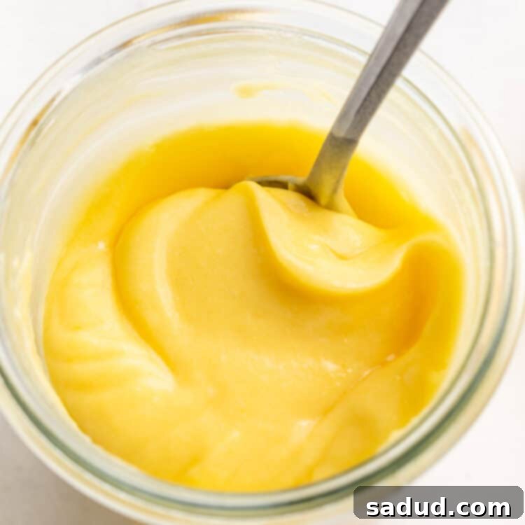 Effortless Keto Lemon Curd Four Ingredients 4 Close-up, overhead view of a glass jar of keto lemon curd with a silver spoon.
