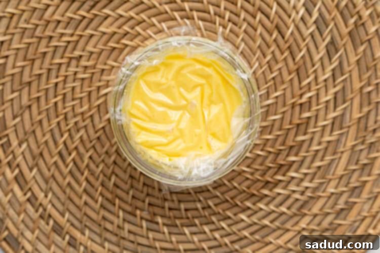 Overhead view of keto lemon curd in a glass jar covered with plastic wrap.