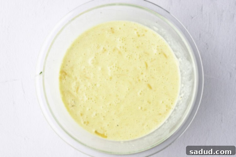 Overhead view of cheese, egg, and cream mixture for a keto breakfast casserole in a glass mixing bowl.