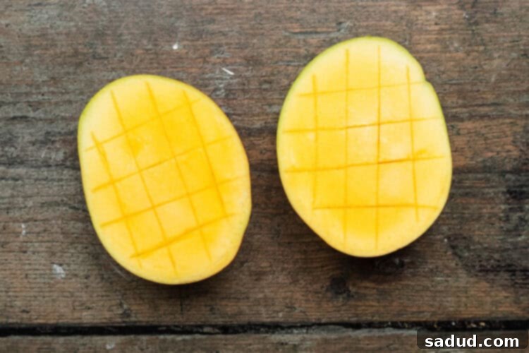 Overhead view of halved and scored mangoes on a baking sheet.