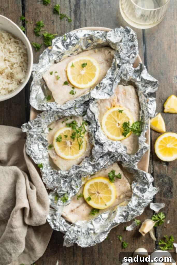 Overhead view of grilled cod in foil with lemon coins and lemon butter sauce.