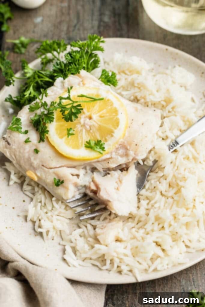 Close-up view of a grilled cod fillet with lemon on a plate with a bed of rice and green garnish.