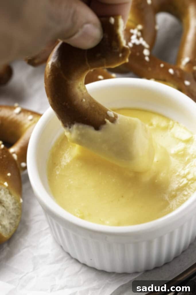 From Freezer to Fantastic: Air Fryer Pretzels 3 A piece of a salted, twisted, air fryer frozen pretzel being dipped into a small ramekin of cheese sauce.