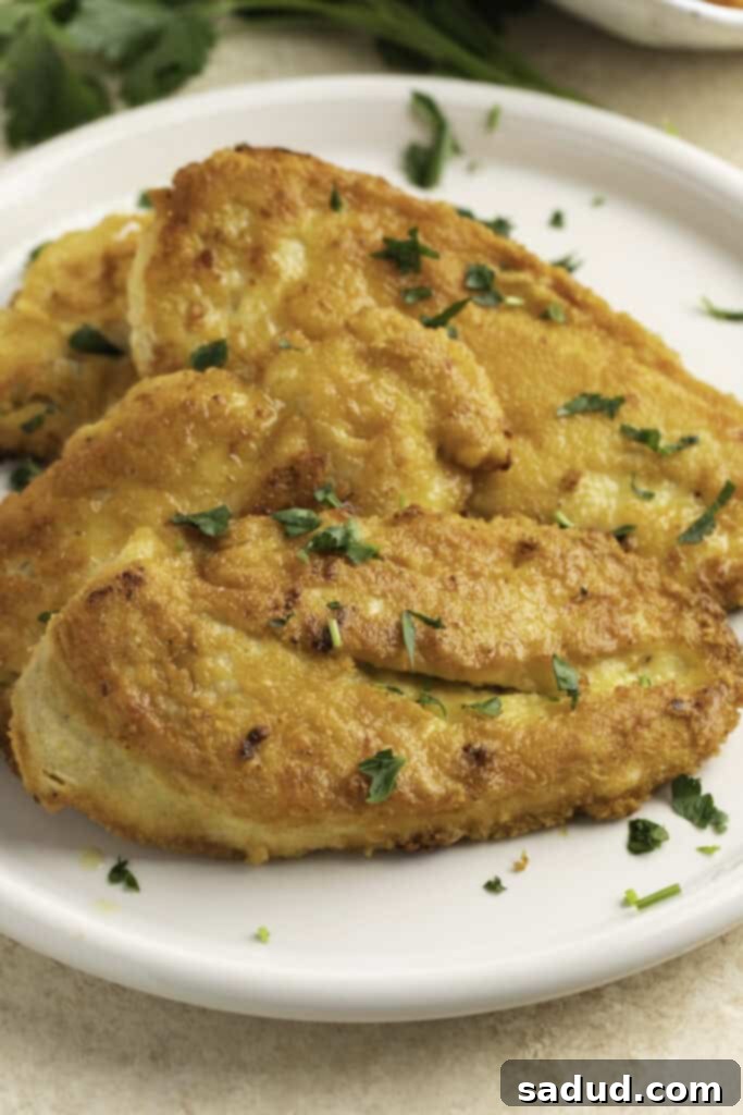 Close-up view of Crusted Chicken Romano on a white plate, showcasing the crispy golden breading and fresh parsley garnish.