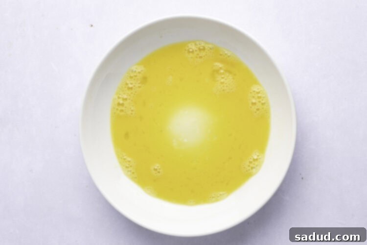 Overhead view of an egg wash in a large shallow bowl, perfectly whisked and ready for dipping.