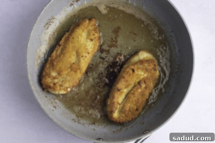 Overhead view of two perfectly fried chicken cutlets in a large skillet, displaying their golden brown and crispy crusts.