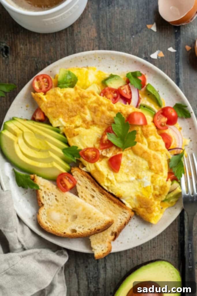 An inviting overhead shot of a freshly prepared avocado omelette served on a plate, accompanied by perfectly toasted bread, bright cherry tomatoes, finely sliced red onions, extra avocado slices, and a sprinkle of fresh herbs.