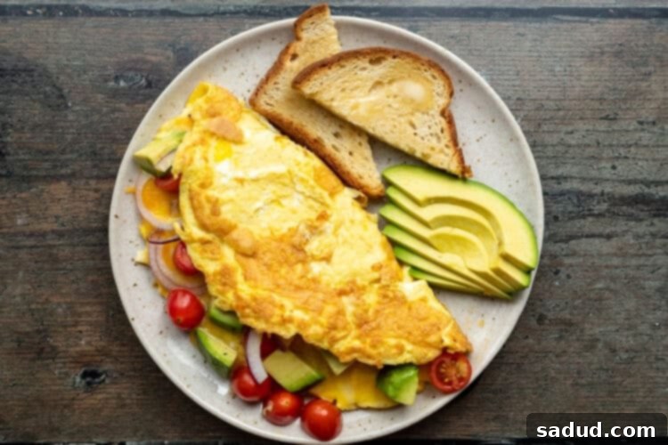 Overhead view of an avocado omelette folded on a white plate with additional tomatoes and avocado.