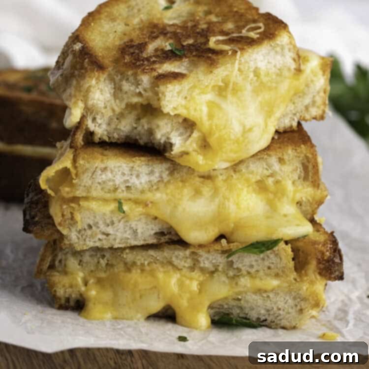 Side view of three halves of sourdough grilled cheeses stacked on top of each other with cheese oozing out.