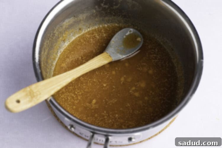 Overhead view of garlic butter sauce in silver saucepan with large spoon.