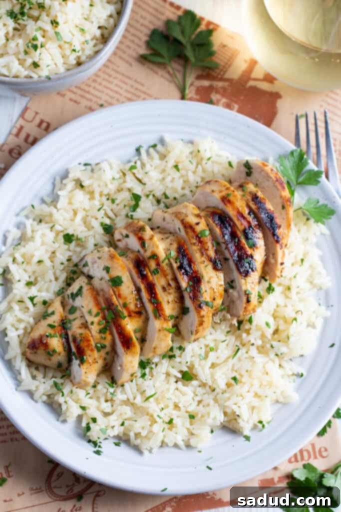 Overhead view of grilled chicken and rice on a white plate, garnished with fresh parsley.