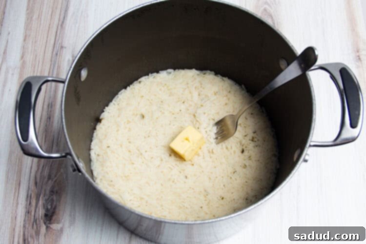 Cooked rice with a pat of butter in a large pot with a fork.