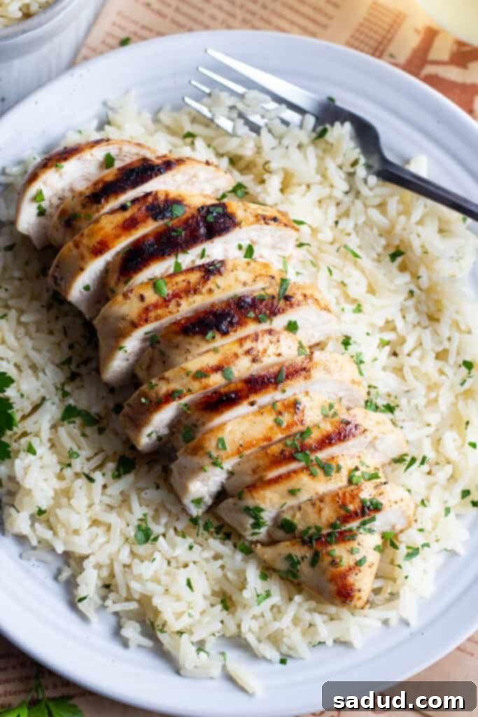 Close-up of grilled chicken on a bed of rice on a white plate, with a fork.