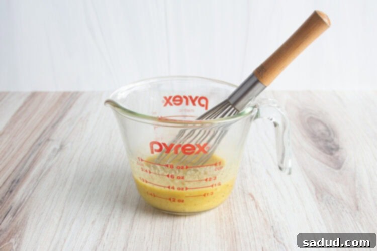 Ingredients for chicken marinade in glass measuring cup with wooden-handled whisk.