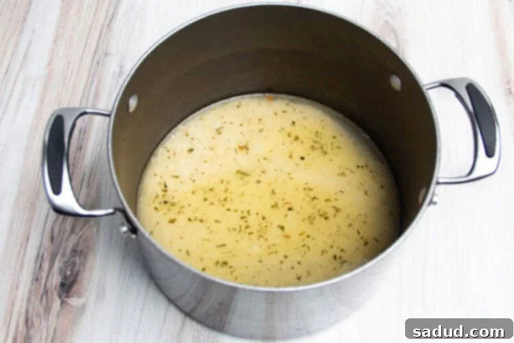 Overhead view of rice with chicken broth in large pot on neutral background.