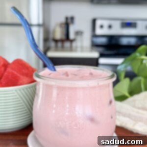 A vibrant pink strawberry watermelon protein yogurt smoothie, garnished with fresh fruit, in a tall glass, set against a bright summer background.