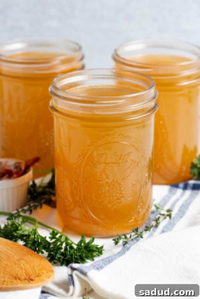 Side, angled view of 3 mason jars of shrimp stock on a title surrounded by fresh herbs and a dish towel.