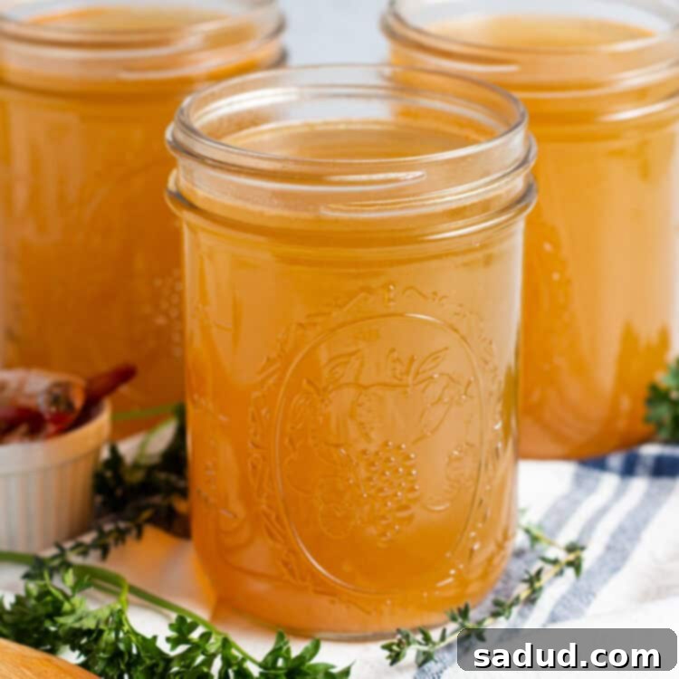 Side, angled view of 3 mason jars of shrimp stock on a title surrounded by fresh herbs and a dish towel.