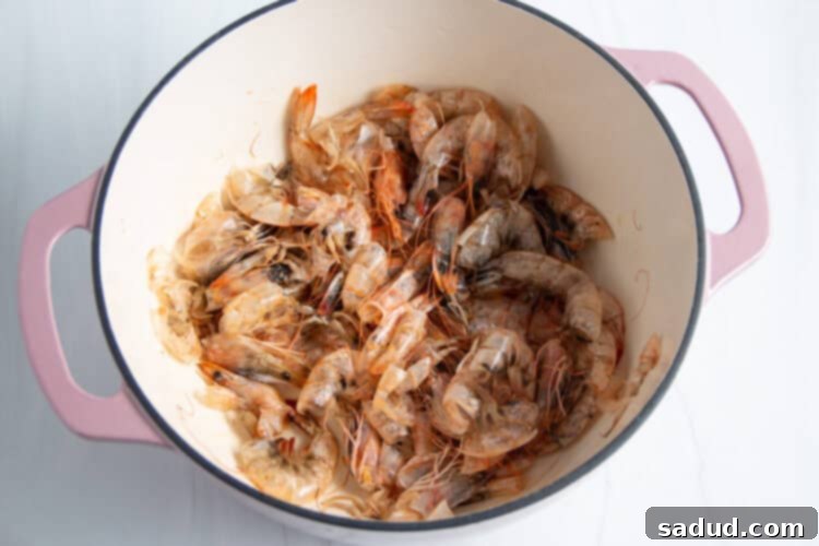 Overhead view of shrimp shells and avocado oil in a large dutch oven on a neutral background.