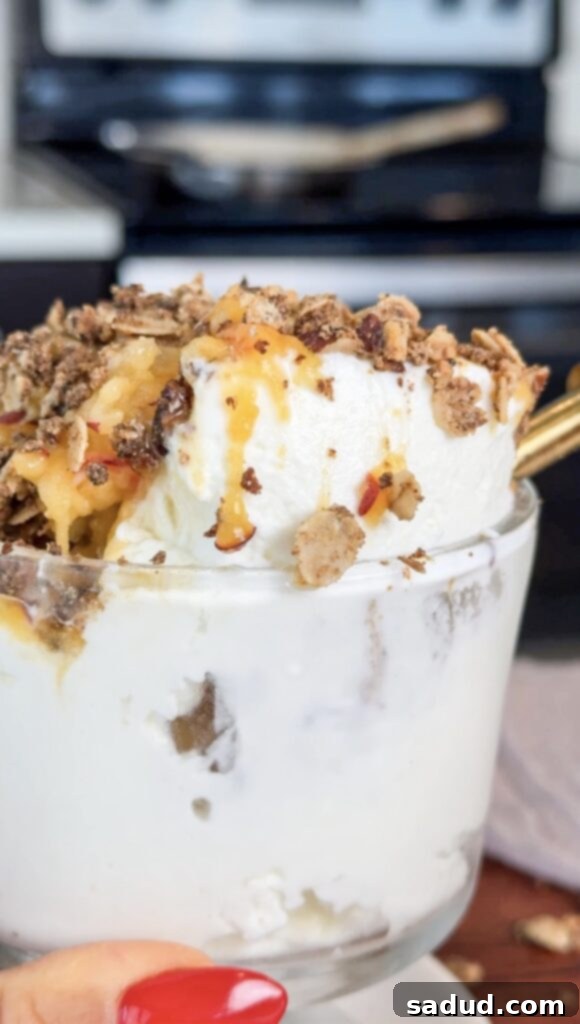 A close-up shot of a finished healthy frozen peach crisp in a glass cup, showing layers of yogurt, shaved peaches, and oat crisp.