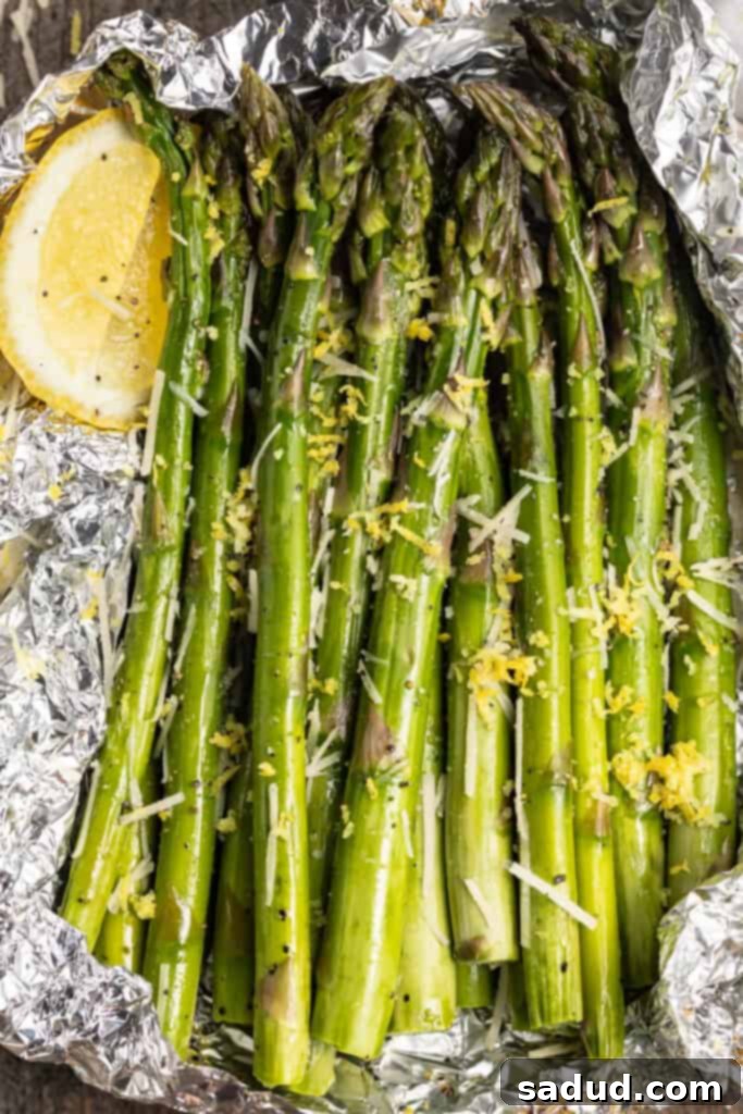Overhead view of grilled asparagus wrapped in foil with lemon wedges, lemon zest, and parmesan cheese, ready to be served.