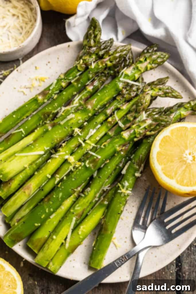 Overhead view of grilled asparagus on a plate with lemon wedges, lemon zest, and parmesan cheese, ready for serving.