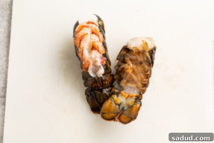 Overhead view of two lobster tails on a cutting board, with one flipped over to show ribs underneath tail.