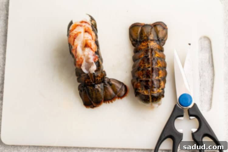 Overhead view of 2 lobster tails on a white cutting board, showing how to pull lobster meat out of one tail for butterflying.