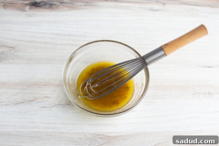 Overhead view of olive oil marinade for grilled broccolini in a glass mixing bowl, perfectly combined.