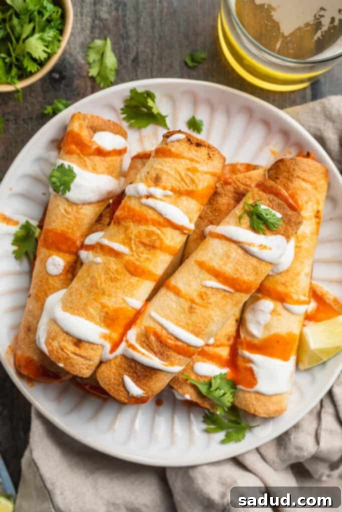 Overhead view of air fryer flautas topped with sour cream and hot sauce on a white paper plate with garnish.