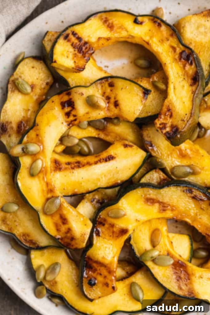 Close-up, overhead view of grilled acorn squash slices on a white plate on a neutral background.