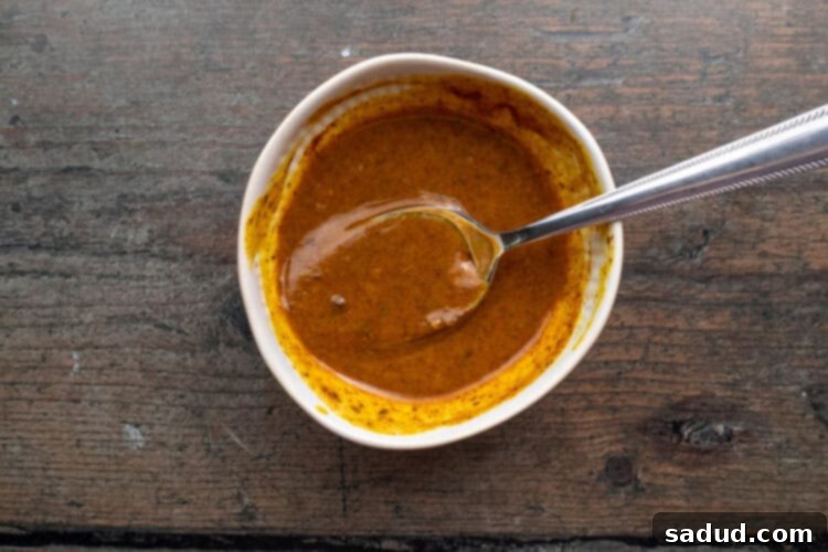 Overhead view of smoky mustard sauce in a small white bowl with a silver spoon.
