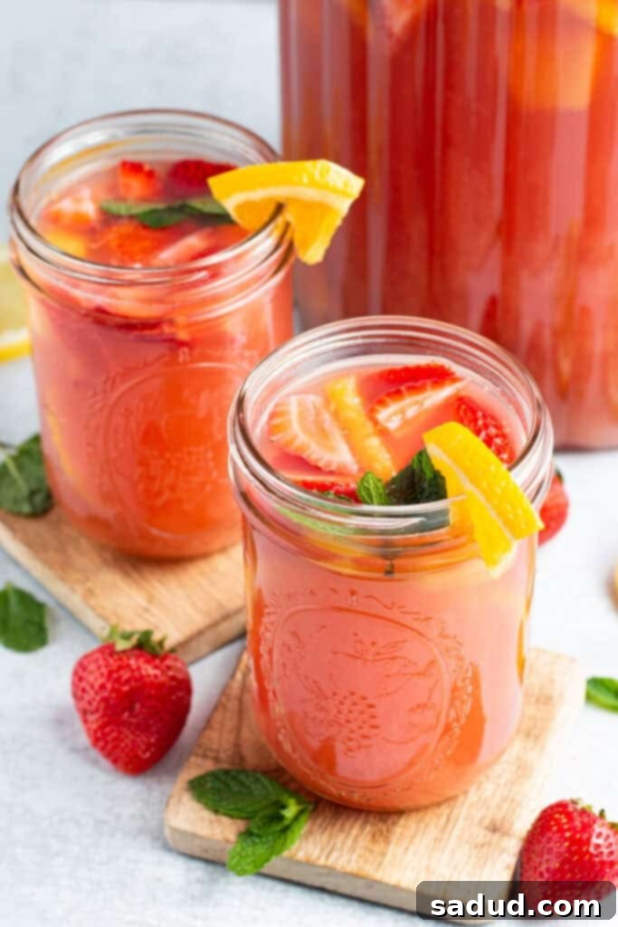 The Ultimate Party Elixir 3 Overhead, angled view of 2 mason-jar-style glasses of bright red jungle juice garnished with fruit.