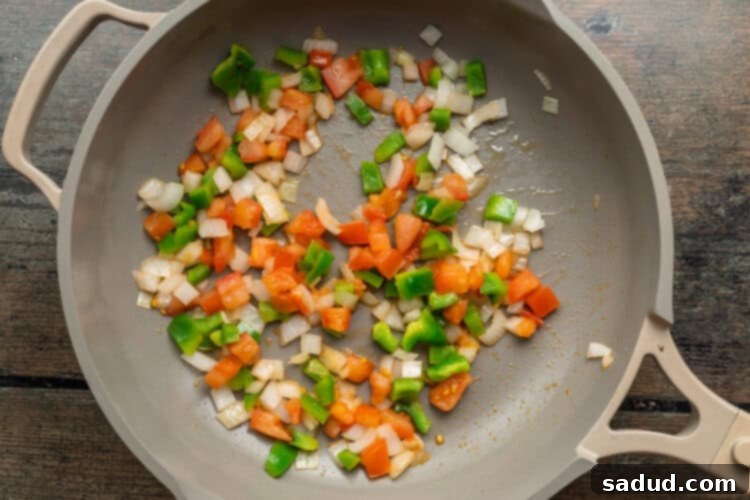 Overhead view of a large skillet containing sautéed onions, green bell peppers, and roma tomatoes.